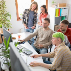 a group of young adults working together at a desk with computers on it