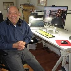 Bill Taube sits at his computer with his adaptive keyboard and large monitor