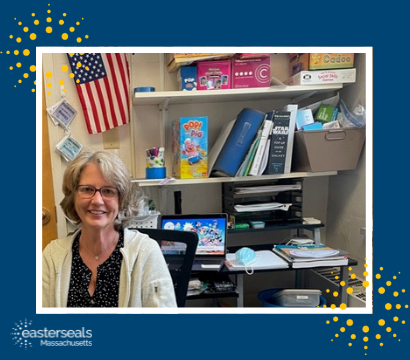 Doris smiles in her office, with a stack of games/tools used during services behind her