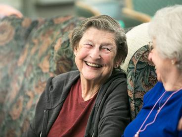Two older adults smiling at each other while sitting on a couch