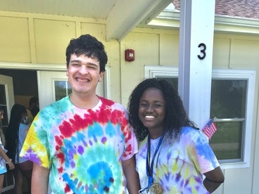 Young adult male with a disability wearing a tie dye tshirt standing with camp counselor