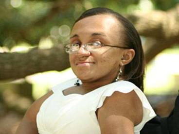 Vilissa Thompson in a white blouse and glasses, in a wheelchair, in a sunny park
