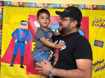 father holding son, with superman drawing on the wall behind them