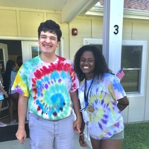 Young adult male with a disability wearing a tie dye tshirt standing with camp counselor