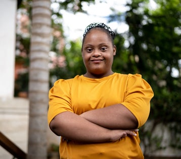 Portrait of a young woman with Down syndrome, arms crossed, determined smile