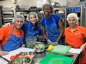 A group of people wearing aprons pose around a table with prepped food