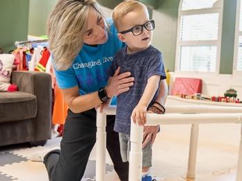 Luke, a young boy, works with an Easterseals therapist using supports to walk