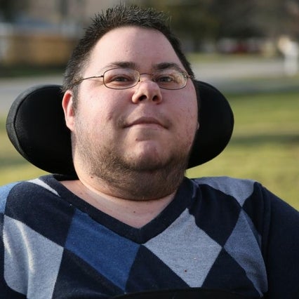 Dom sitting in their wheelchair outside