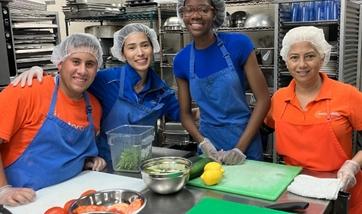 A group of people wearing aprons pose around a table with prepped food