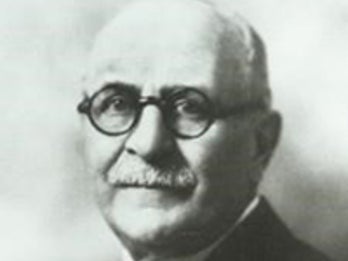 An old photograph of a man looking at the camera. He is wearing circular glasses and a business suit.