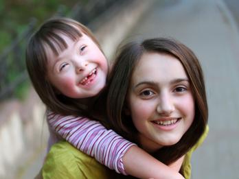 A young smiling girl with Down syndrome gets a piggy back ride