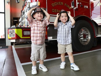 two young boys try on firemen's hats at a fire station