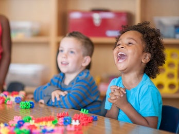 Elementary age children are playing with toy blocks together at a table.