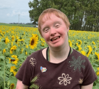 A woman with Down syndrome smiles in a field of sunflowers