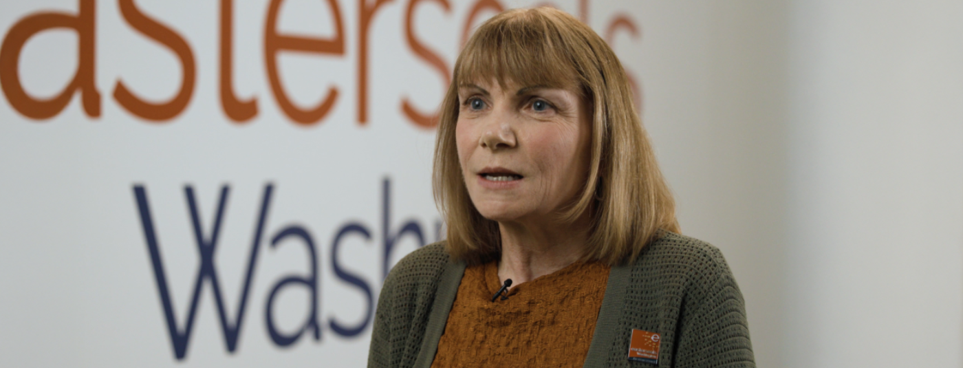 Cathy Bisaillon speaking in front of a wall that has the Easterseals Washington logo on it.