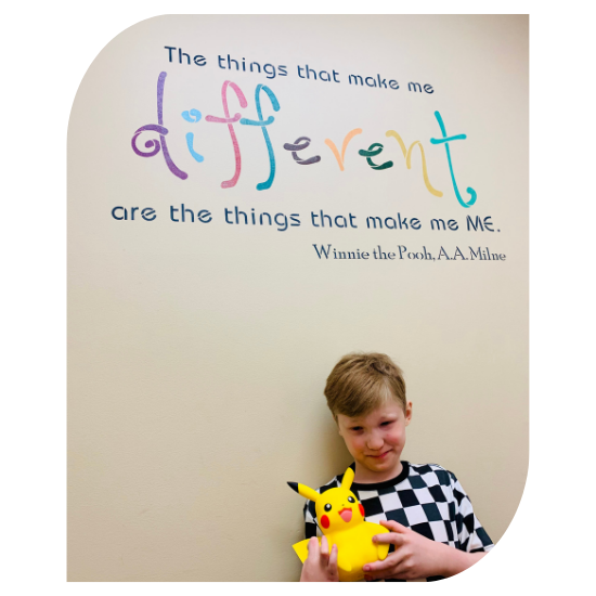 Harrison holds a Pikachu plush and stands below a wall decal that says: "The things that make me different are the things that make me me."